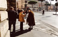 two older Italian women converse on a street corner in Rome with a bus in the background